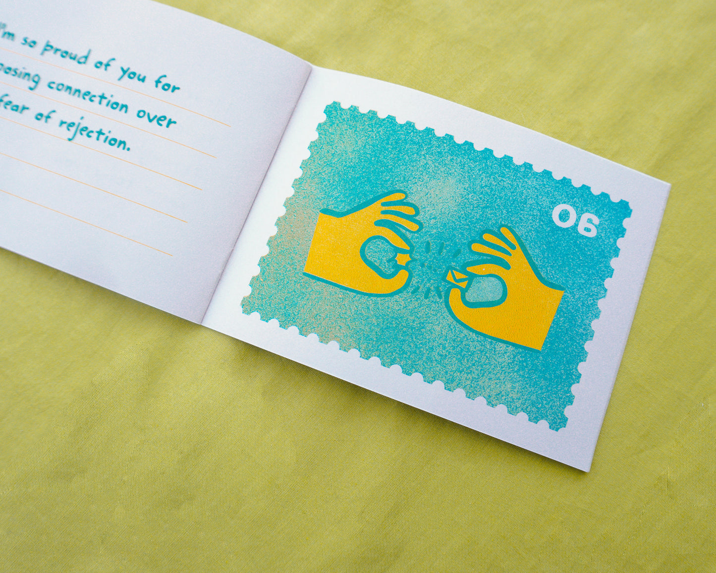 An open zine on a yellow-green textured surface, showing a risograph printed turquoise postage-stamp-style graphic with yellow hand silhouettes and the number 06. The left page has partial handwritten text in blue.