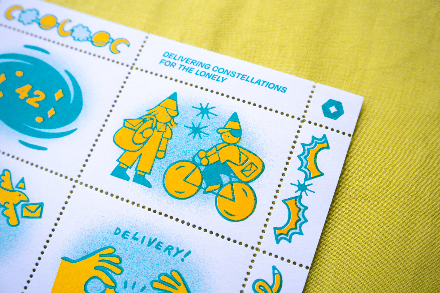 A close-up of a risograph printed postage stamp sheet featuring whimsical illustrations and the text 'DELIVERING CONSTELLATIONS FOR THE LONELY' on a textured yellow background.